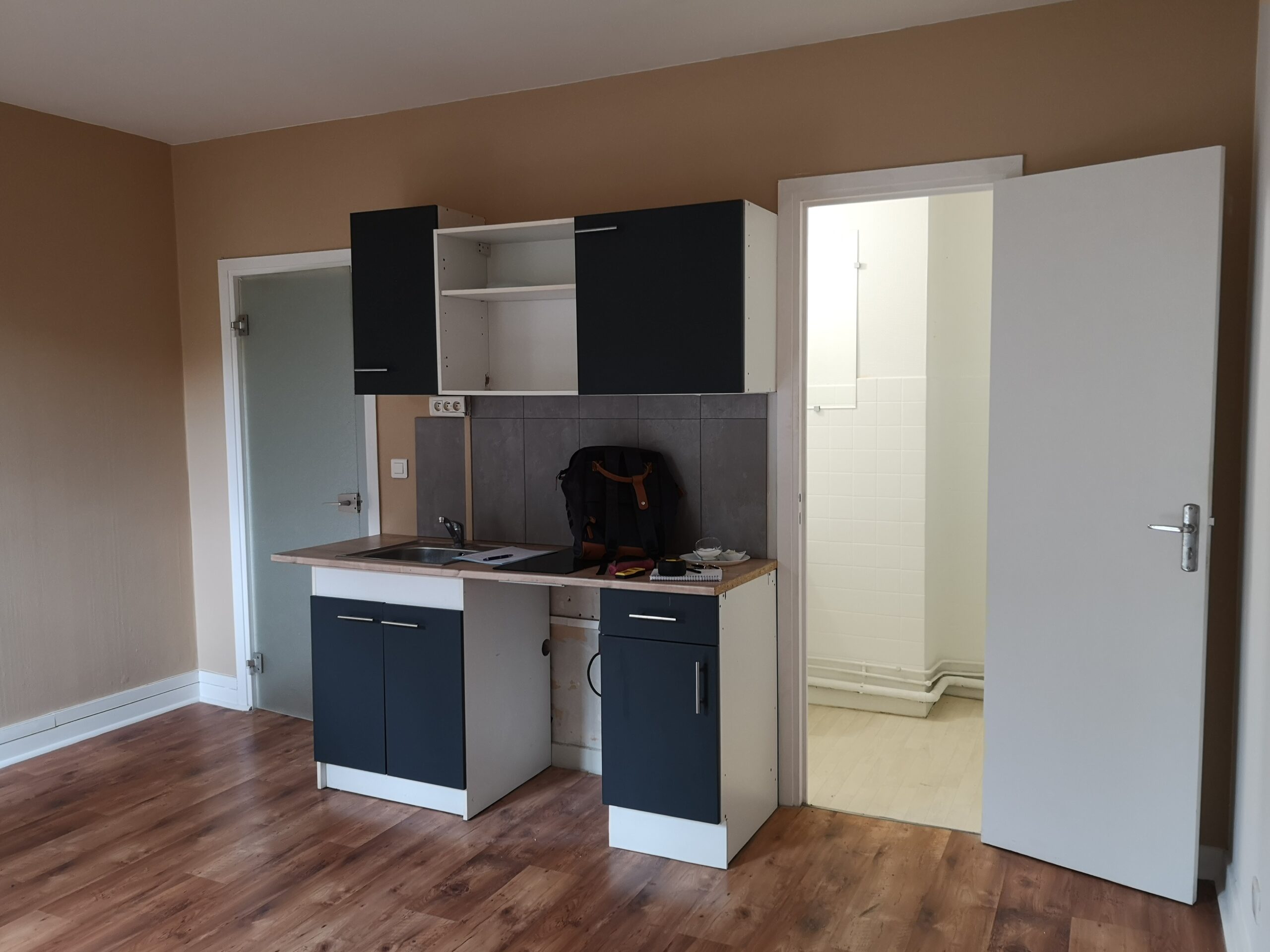Studio étudiant : coin cuisine avant aménagement, les portes des meubles sont foncées