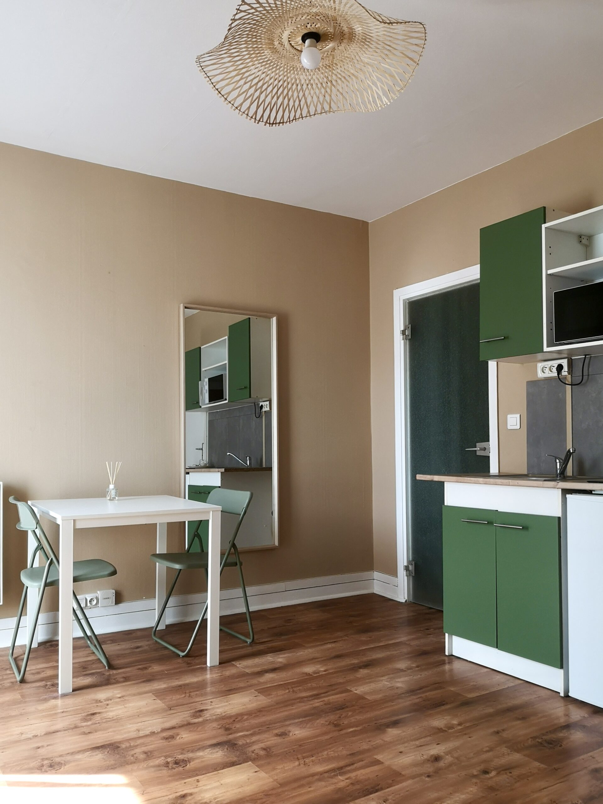 Aménagement du studio étudiant : coin repas avec une table deux personnes, les meubles sont repeints en vert et un réfrigérateur et un microondes sont installés