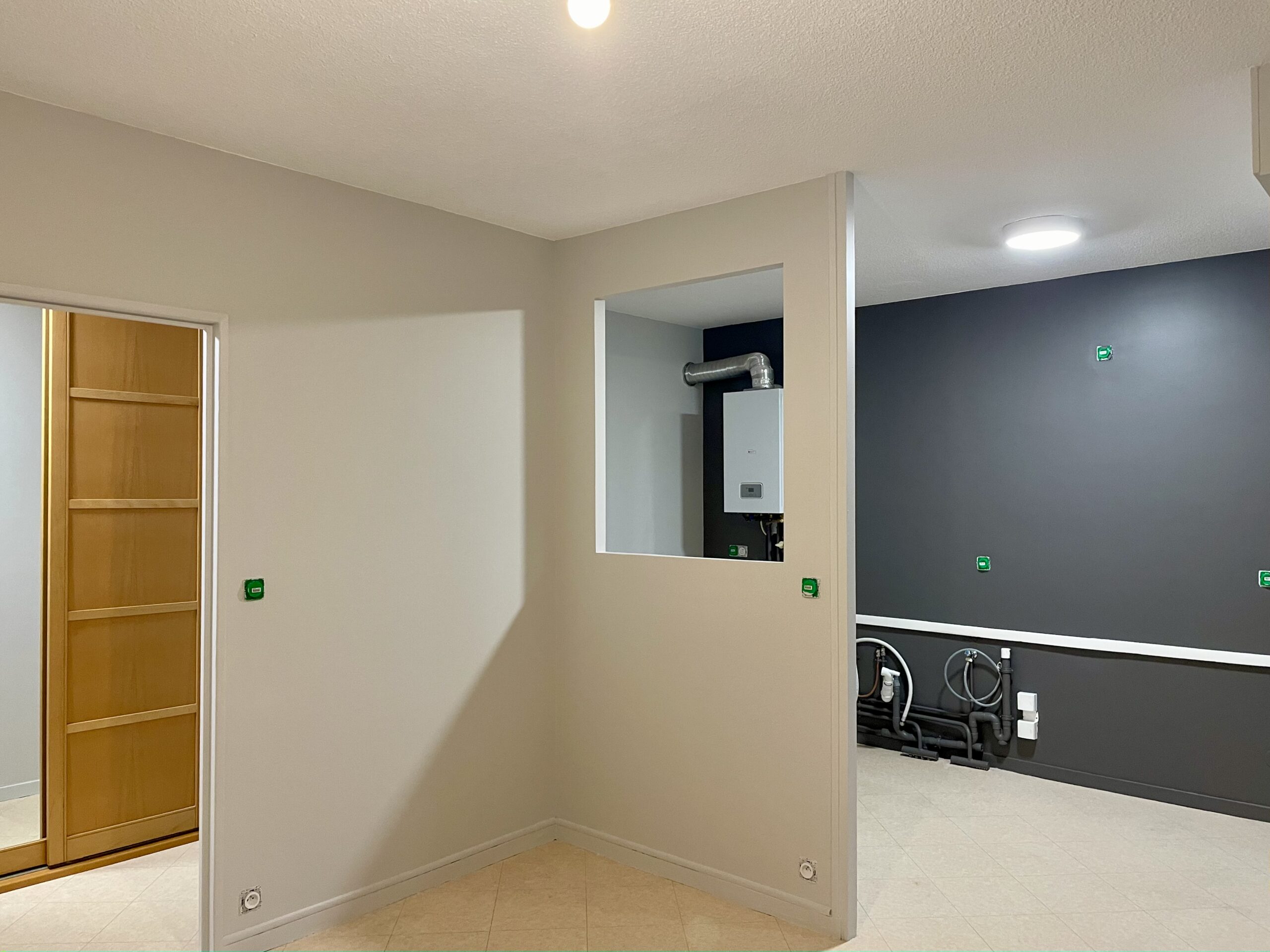 pièce de vie après travaux, la cuisine est ouverte sur le salon, une ouverture a été créée dans le mur de séparation entre les deux pièces, vue depuis le salon